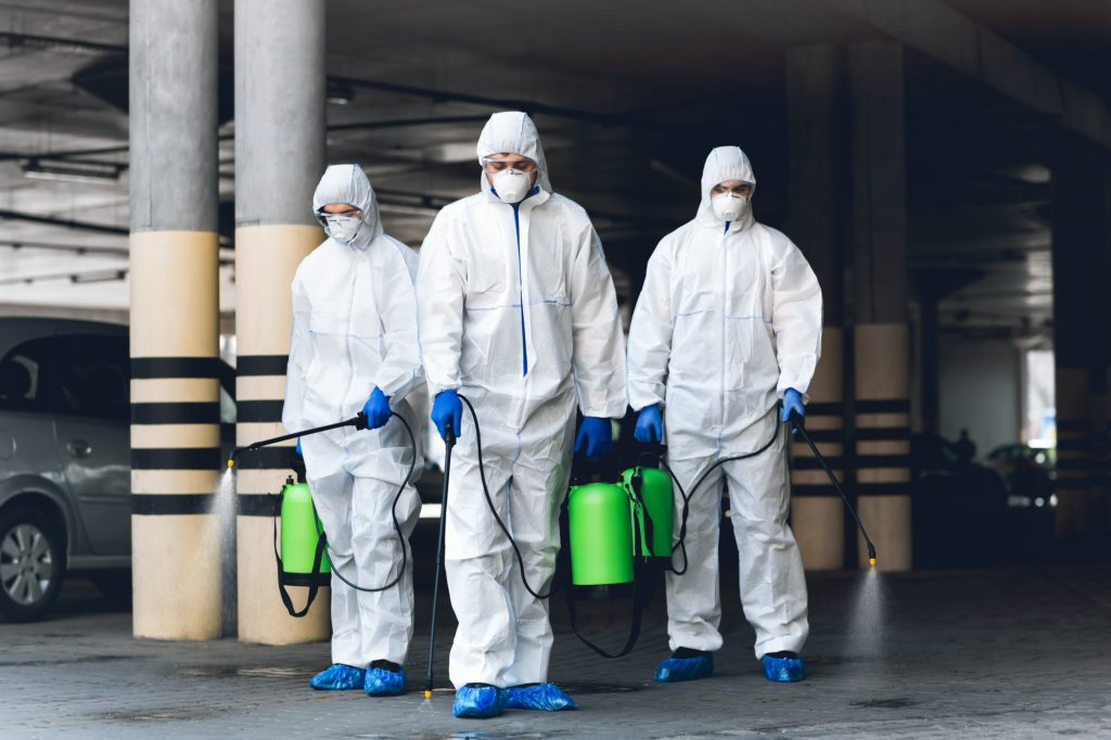 Virologists wearing hazmat suits disinfecting parking with spray chemicals